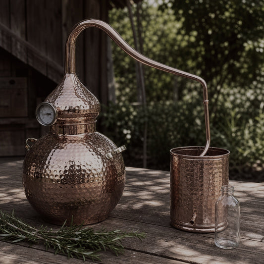 Copper alembic still set up outdoors with fresh rosemary for essential oil and hydrosol