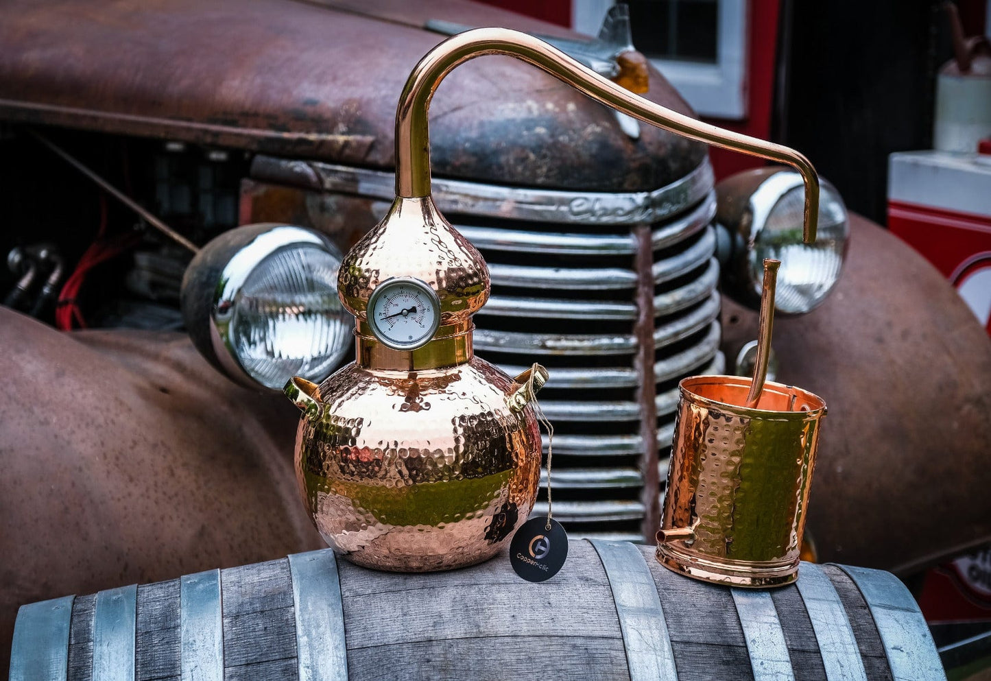 5-Litre Copper Alembic Still mounted on oak barrel, featuring ornate hammered copper pot and coiled condenser arm